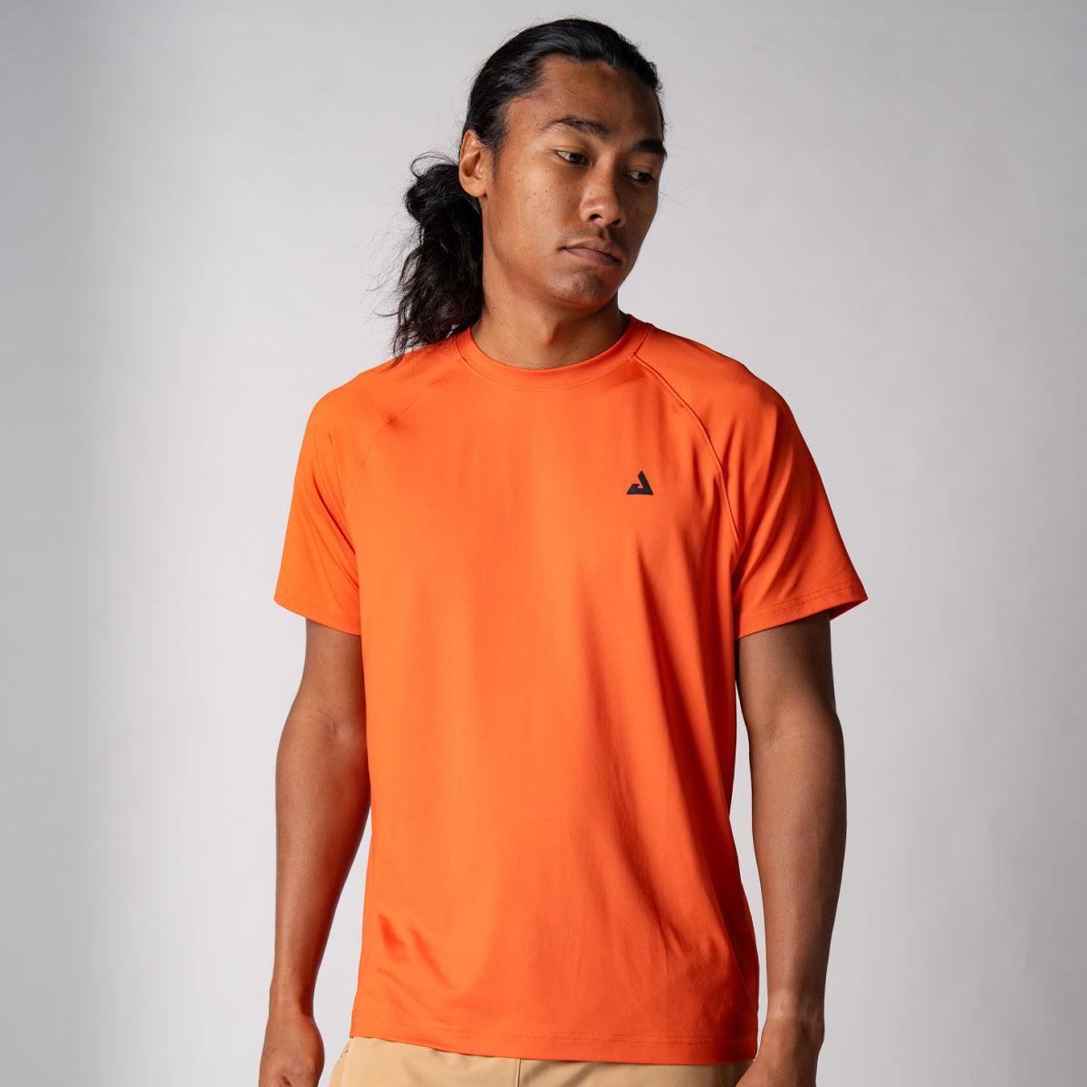 Mann trägt orangefarbenes, kurzärmeliges Sport-T-Shirt mit kleinem schwarzem Logo auf der Brust vor grauem Hintergrund.