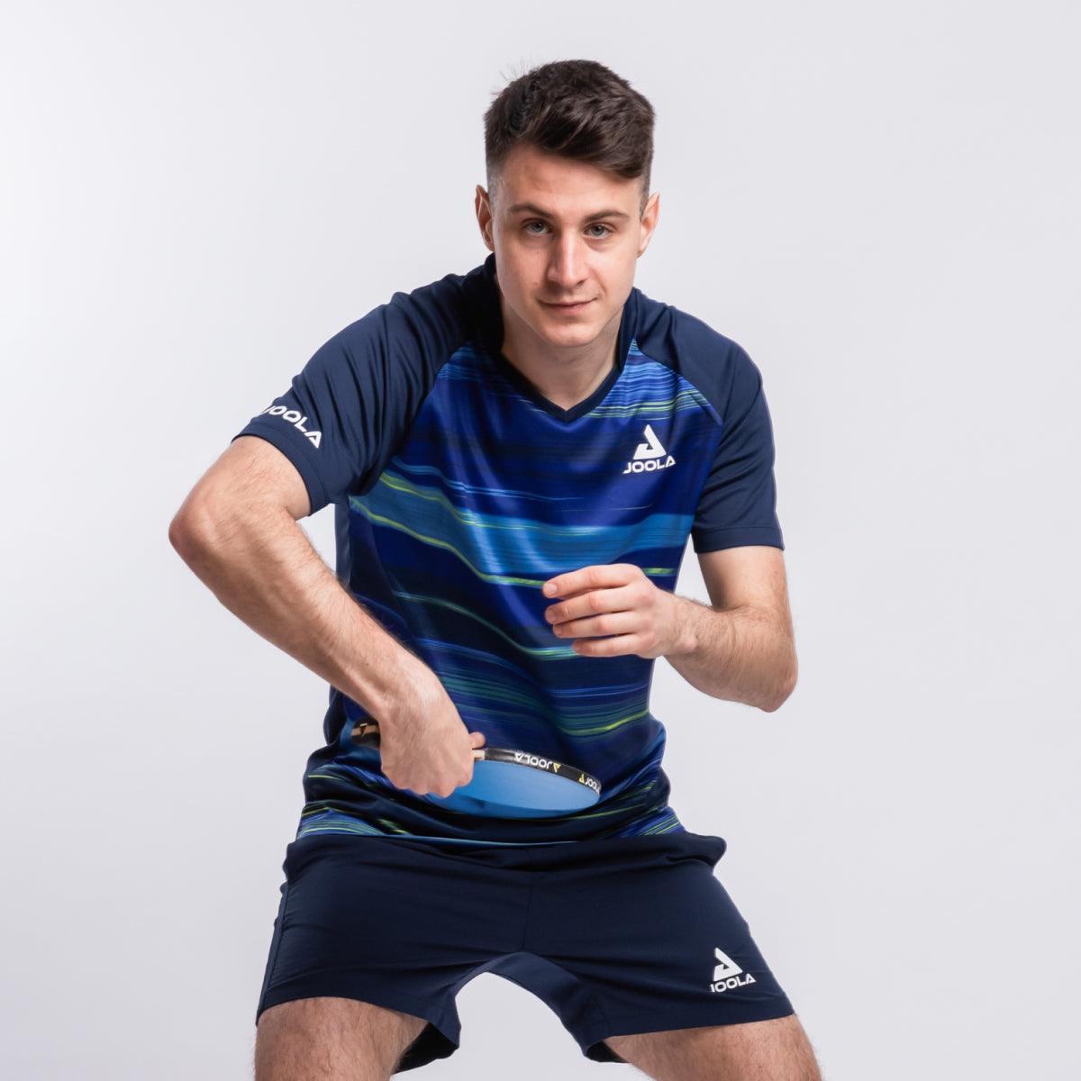 Junger Mann in blauem JOOLA Tischtennis-Outfit hält Tischtennisschläger in Spielposition.