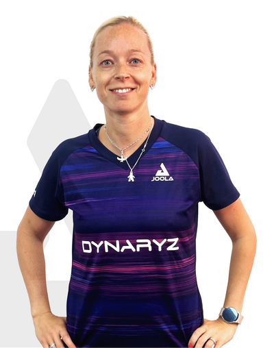 Frau trägt blau-lila JOOLA Sportshirt mit DYARYZ-Logo, silberne Ketten, Armbanduhr und steht vor weißem Hintergrund.