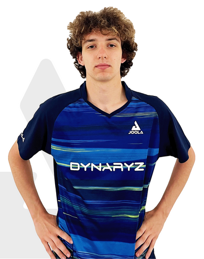 Junger Mann mit blauem JOOLA Dynaryz Sportshirt mit Streifenmuster, Hände in die Hüften gestützt, vor weißem Hintergrund.