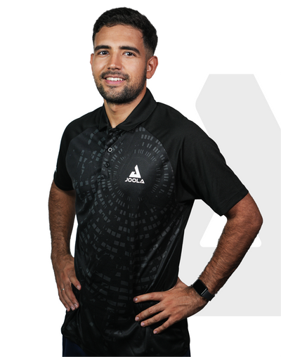 Mann trägt schwarzes JOOLA Polo-Shirt mit Muster, steht mit Händen in der Hüfte, lächelt, weißer Hintergrund.