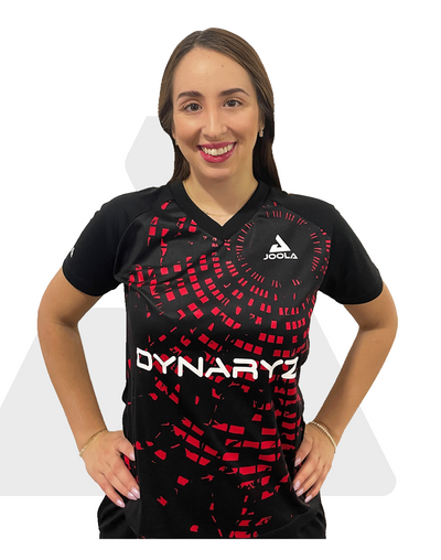 Frau trägt schwarzes JOOLA Sportshirt mit rotem Muster und weißem DYNARYZ Schriftzug, lächelnd, Hände in Hüfte.