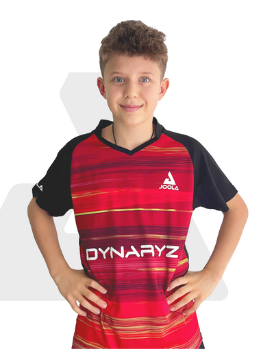Junge mit rotem JOOLA Tischtennis-Trikot mit schwarzen Ärmeln und DYNA RYZ Schriftzug, Hände in der Hüfte.