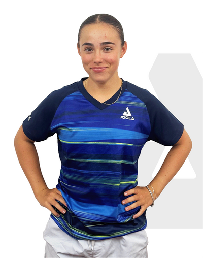 Frau trägt blaues JOOLA Sportshirt mit Streifenmuster und weißer Hose, Hände in die Hüften gestützt.