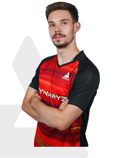 Mann mit rotem und schwarzem JOOLA Sportshirt mit DYNAAYZ-Logo, Arme verschränkt, vor weißem Hintergrund.