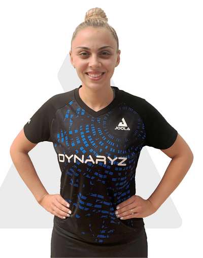 Frau mit hochgestecktem blondem Haar trägt schwarzes JOOLA Dynaryz Sportshirt mit blauem Muster, lächelt.