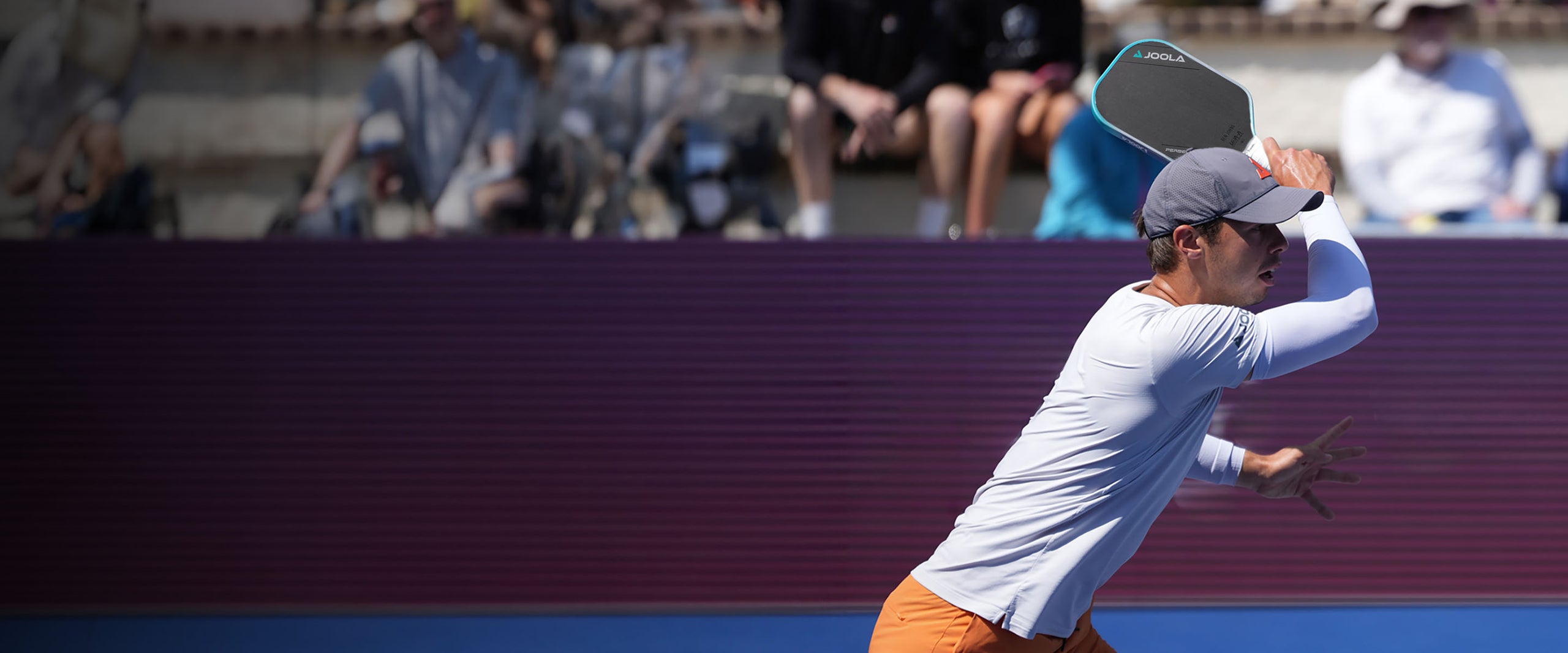 Mann in Sportkleidung spielt Pickleball mit JOOLA-Schläger auf Outdoor-Platz vor Zuschauern.