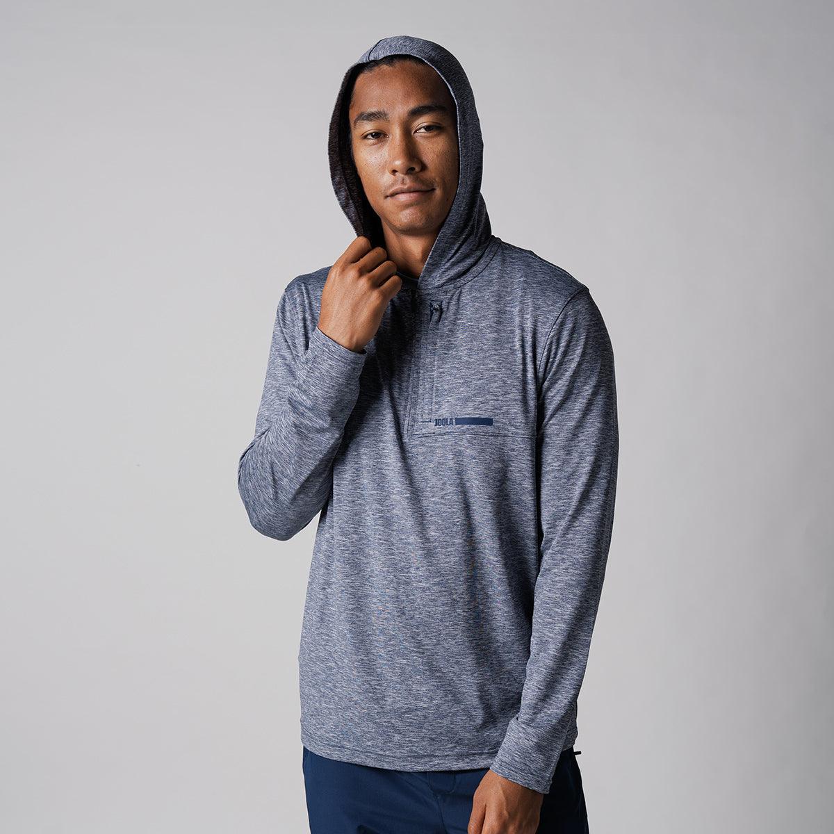 Mann trägt grauen Kapuzenpullover mit langem Arm vor neutralem Hintergrund.
