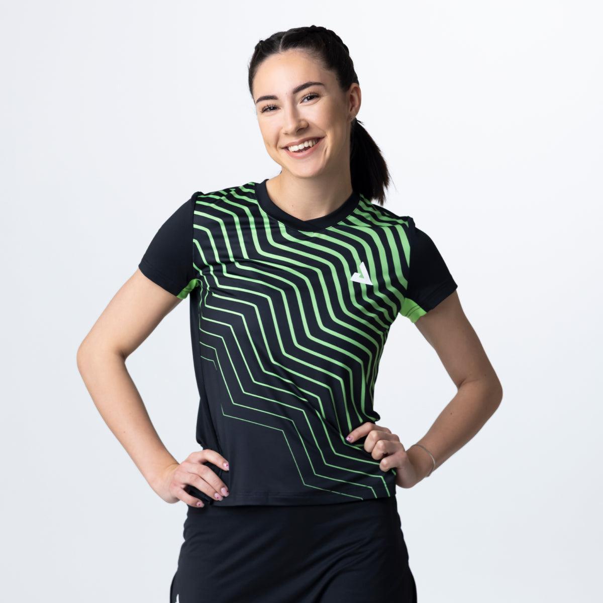Frau trägt schwarzes Sportshirt mit grünem, geometrischem Muster und kurzem Ärmel vor weißem Hintergrund.