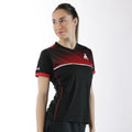 Frau trägt schwarzes Sportshirt mit roten und weißen Akzenten, stehend vor weißem Hintergrund.