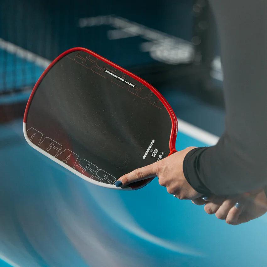 Person hält schwarzen und roten Pickleball-Schläger über einem blauen Spielfeld.