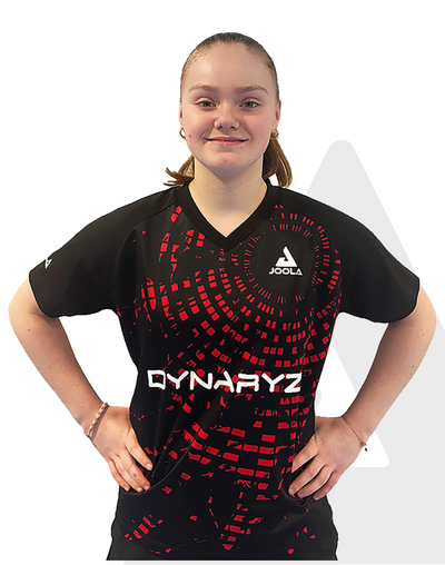 Frau trägt schwarzes JOOLA Dynaryz Sportshirt mit rotem Muster, V-Ausschnitt und kurzen Ärmeln, Hände in der Hüfte.