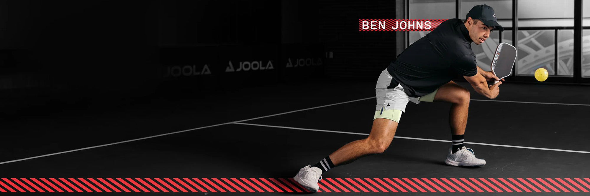 Mann in Sportoutfit spielt Pickleball, hält Schläger und schlägt gelben Ball auf Indoor-Platz.