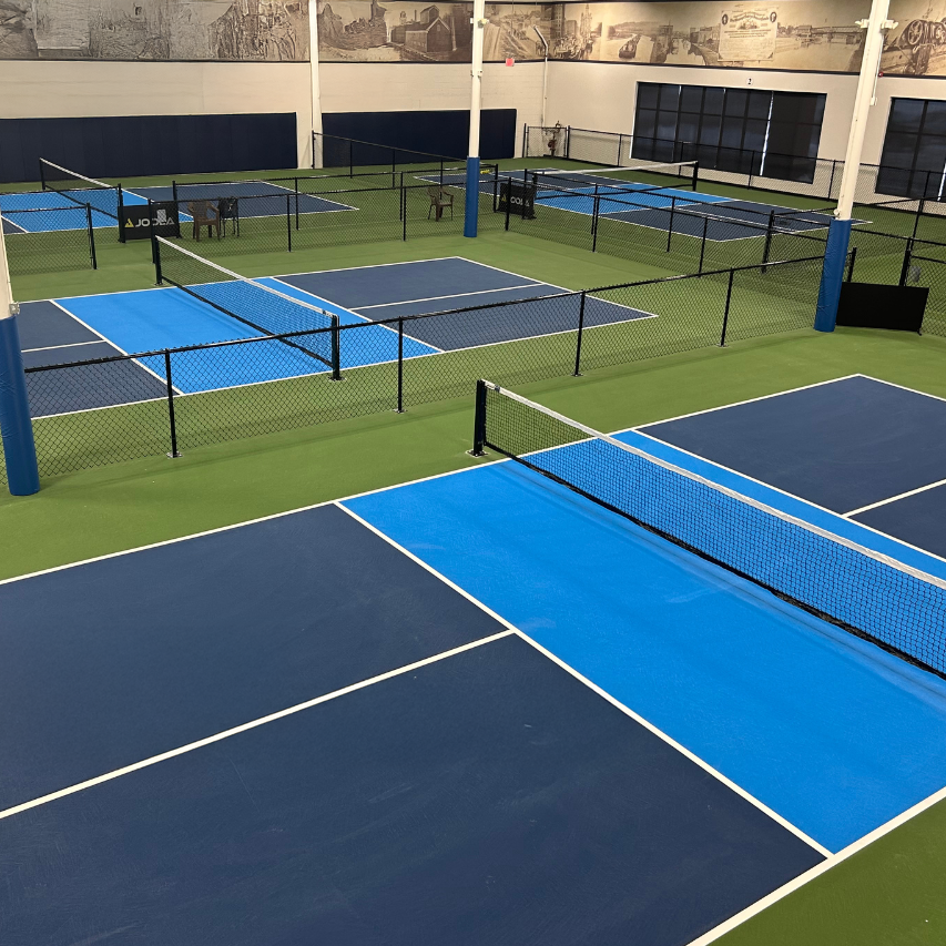 Indoor-Pickleball-Anlage mit mehreren blauen und grünen Spielfeldern, Netzen und Trennzäunen.
